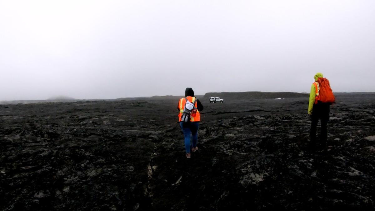 Researcher walks across black Icelandic lava flow.